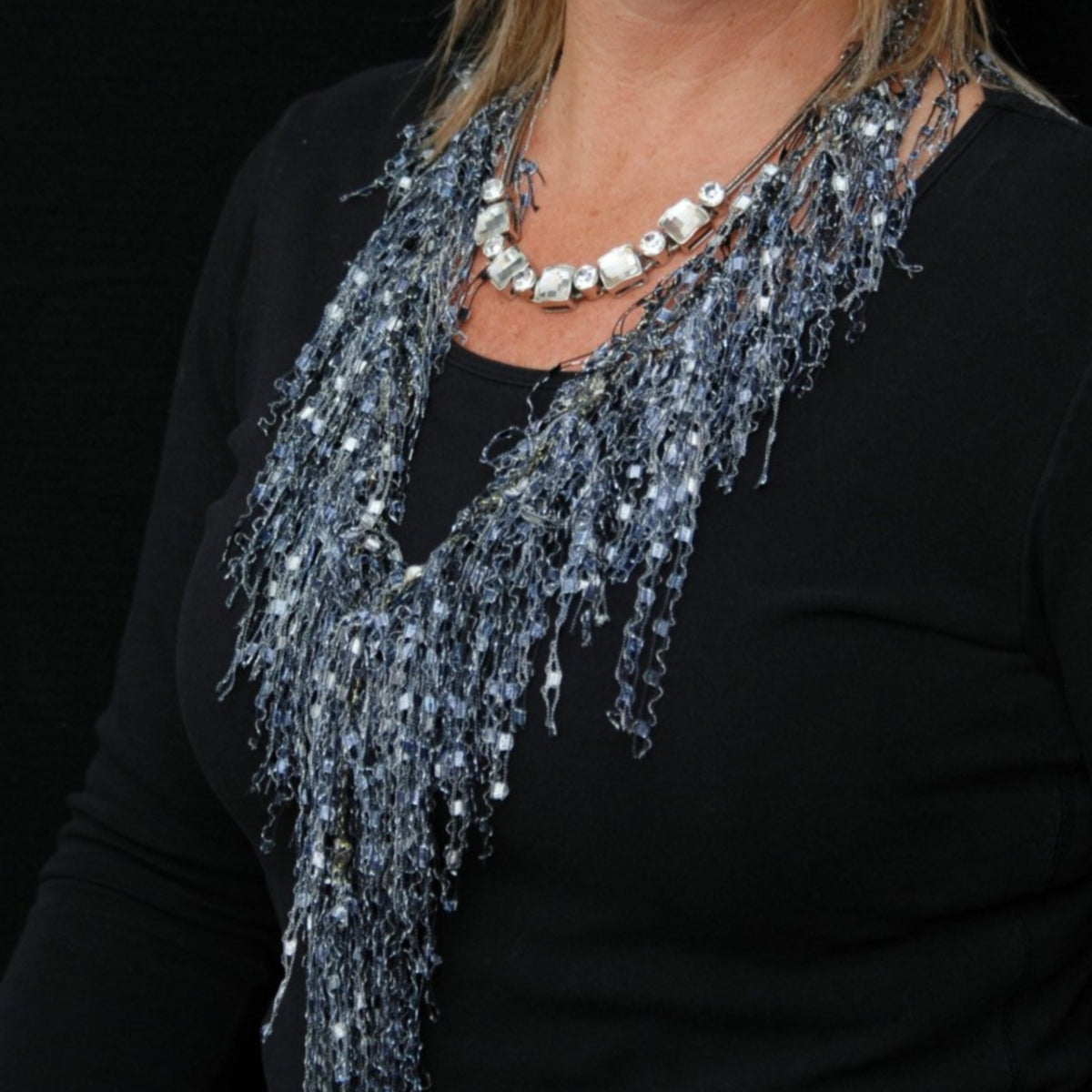 Close up of model wearing black top with silver rhinestone necklace and lack and whit scarf necklace
